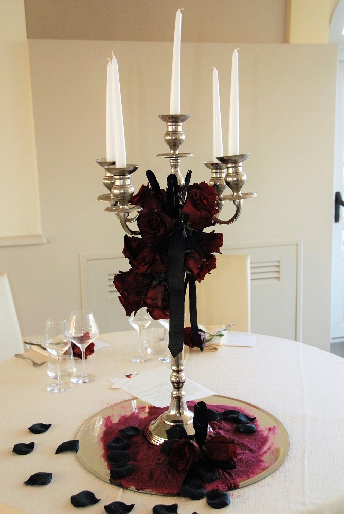 Dracula inspired centerpiece, on the spouses table, with red roses on a candlestick holder and black rose petals
