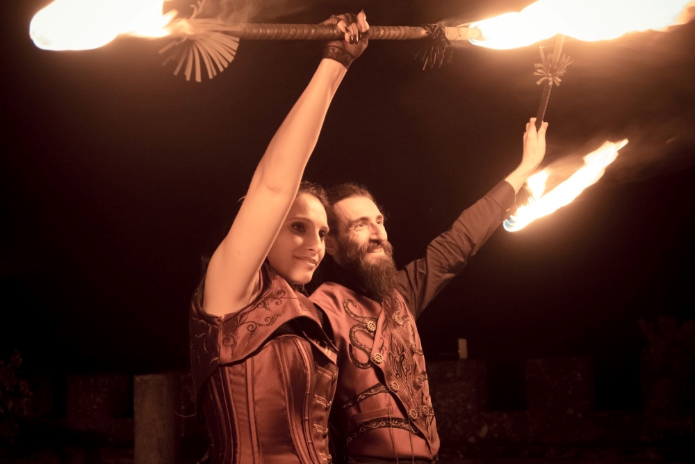 Smiling bride and groom in steampunk style clothing, posing with burning fire show equipment