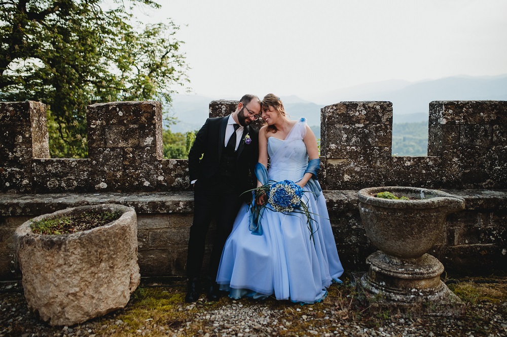 Happy spouses in a castle wedding in tuscany, smiling while sitting on the castle walls