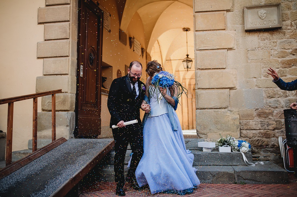 Happy spouses at a wedding in tuscany, walking out the city hall under a shower of petals