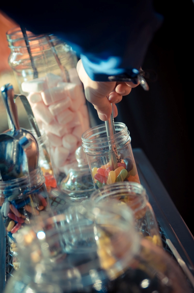 A hand taking jellybeans from a jar, sourrounded by other tall jars full of candy