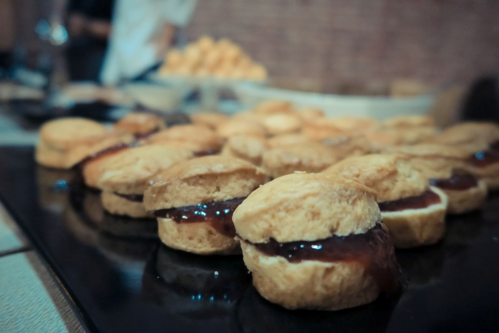 A black tray full of small english tea scones with jam at an open air ceremony