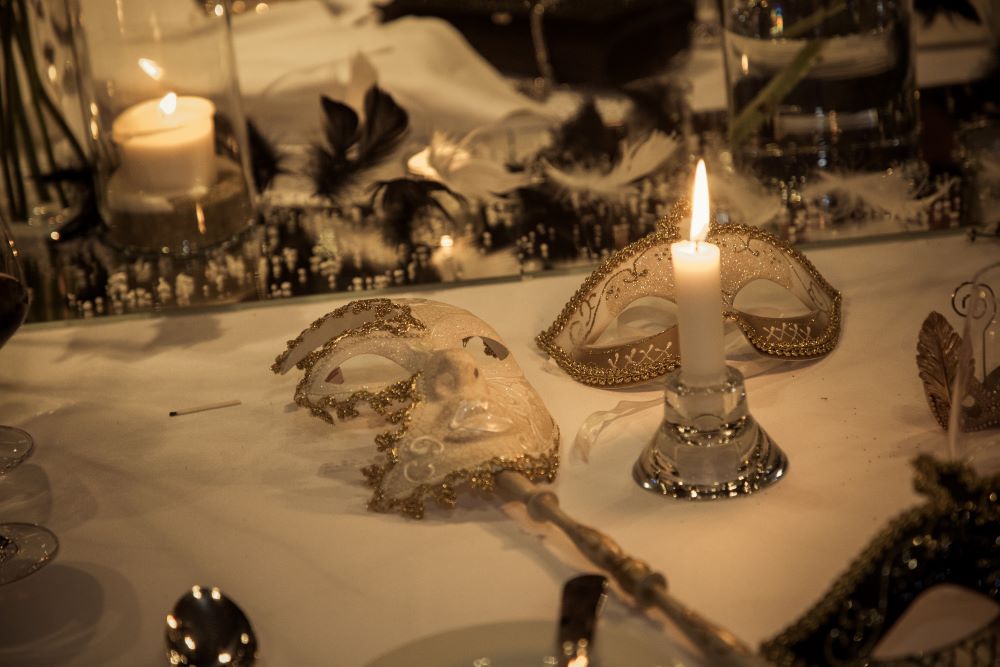 Centerpiece detail, with mirrors, black feathers, candles and two white and gold masks with a burning candle.