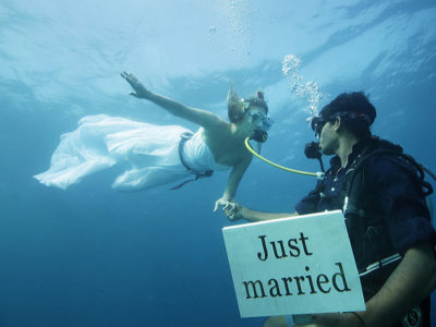 Foto di due sposi sott'acqua, lo sposo ha un cartello 