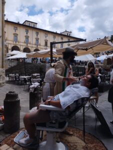 A tourist getting their facial hair shaved in public at the arezzo antiques' fair